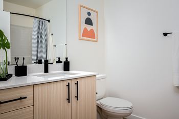 A bathroom with a toilet, sink, and a painting on the wall.
