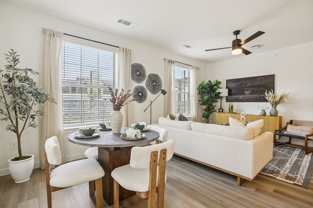 A living room with a white couch, a round table with chairs, and a ceiling fan.