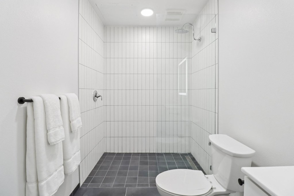 A white toilet sits next to a white sink in a white tiled bathroom.