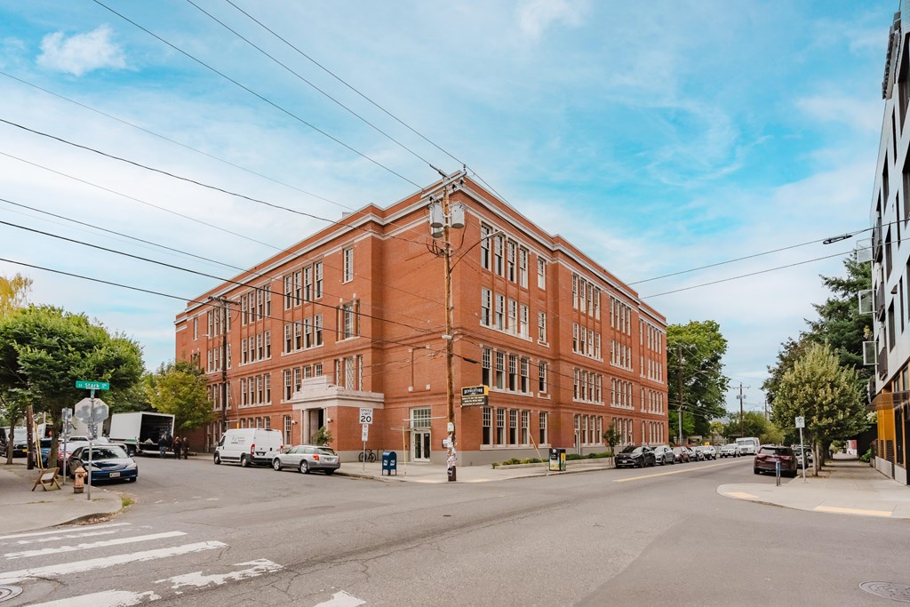 A large red brick building sits on a street corner with cars parked in front.