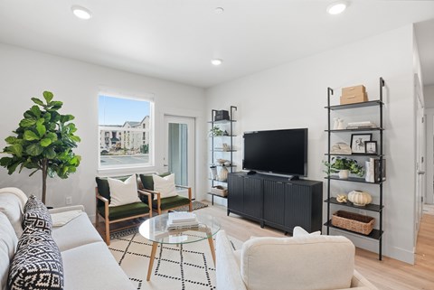A living room with a black sofa, a glass coffee table, and a television on a stand.