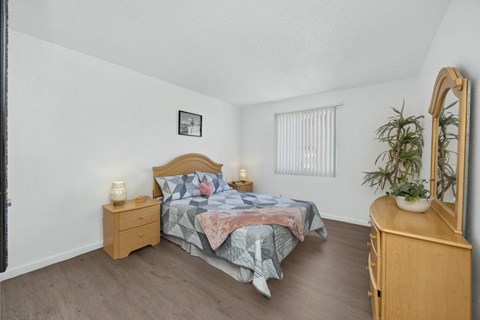 A bedroom with a bed, nightstand, and a plant.