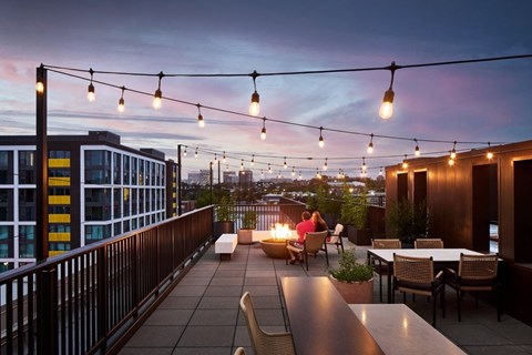 A rooftop patio with people sitting and string lights hanging above.