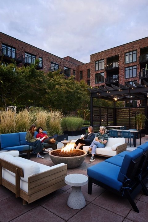 A group of people are sitting around a fire pit on a patio.