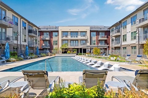 A pool surrounded by chairs and plants in front of apartment buildings.