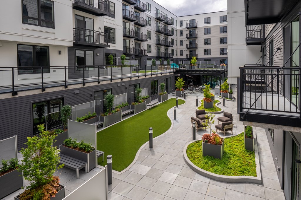 A courtyard with a grassy area and benches surrounded by buildings.