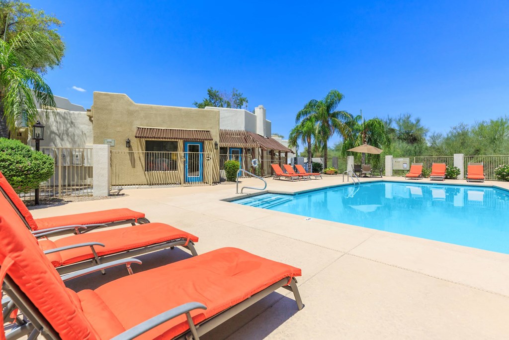 A pool with red sun loungers and a building in the background.