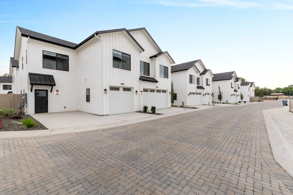 A row of white houses with black roofs and a brick driveway.