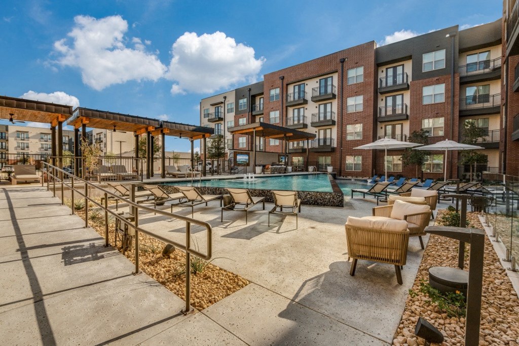 a pool with chairs and umbrellas in front of an apartment building