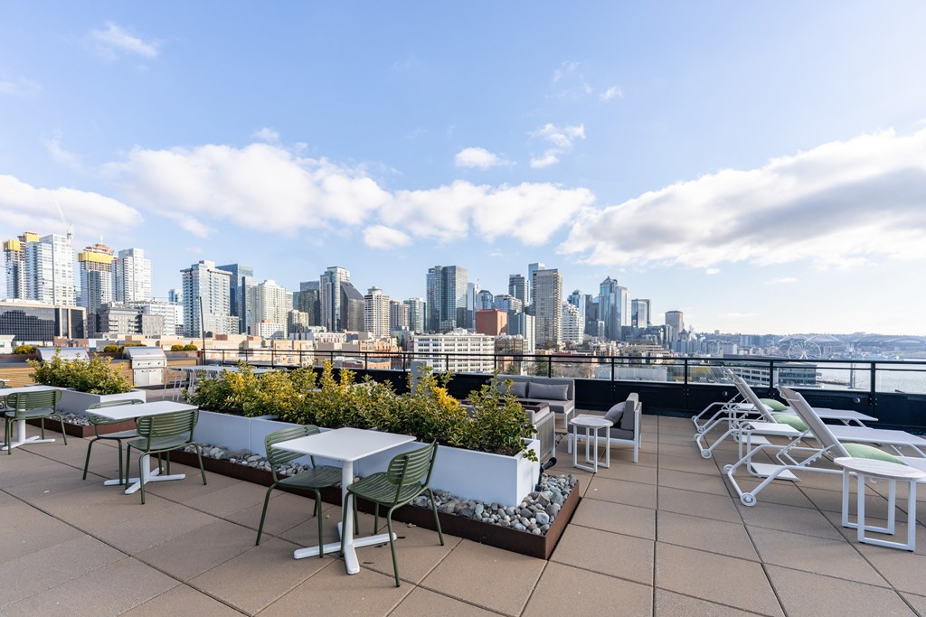A rooftop patio with tables and chairs overlooking a city skyline.