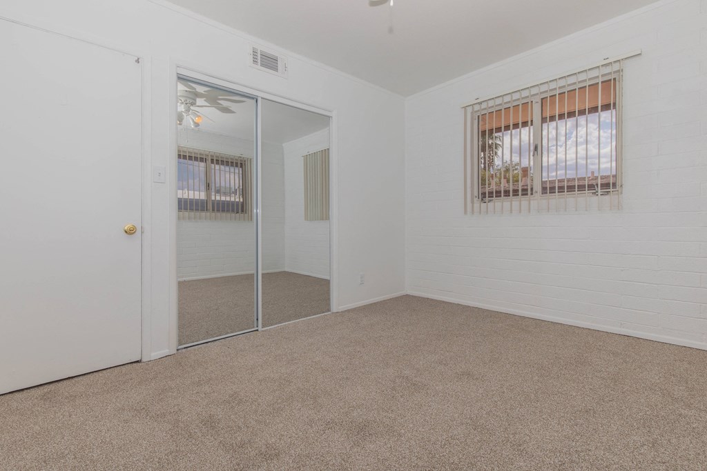 A room with a carpeted floor, a window with blinds, and a sliding glass door.