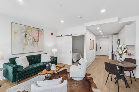 A living room with a green couch, white chairs, and a painting on the wall.