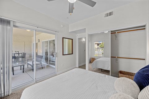A bedroom with a large bed and a sliding glass door leading to a balcony.
