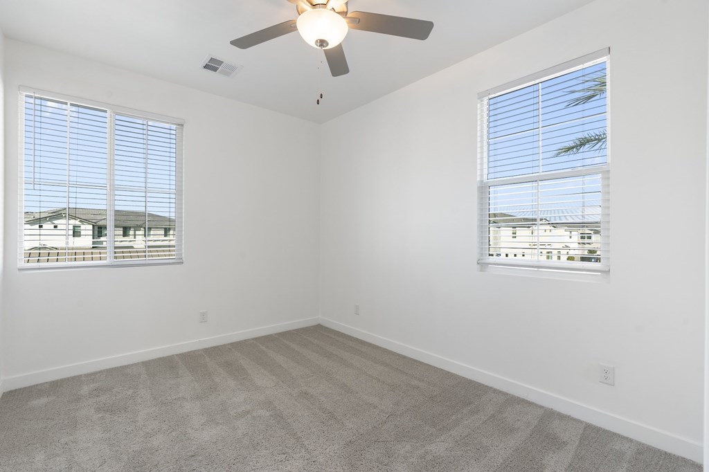A room with a ceiling fan and two windows.