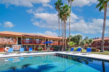 A swimming pool in front of a building with palm trees.