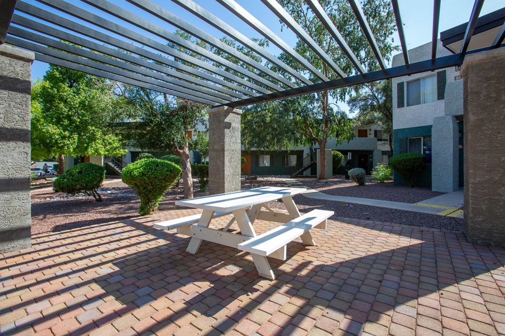 A white picnic table is under a metal awning on a brick patio.