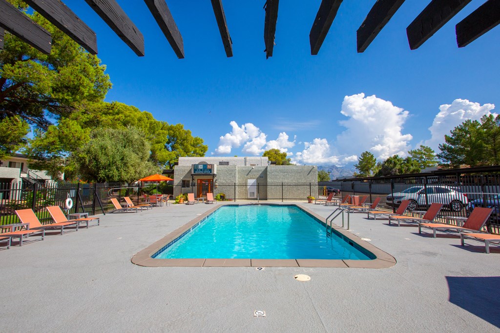 A large swimming pool surrounded by orange lounge chairs and wooden pergolas.