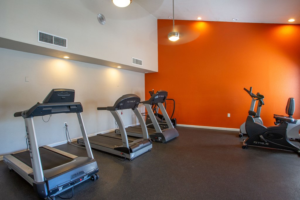 A gym with orange walls and treadmills.