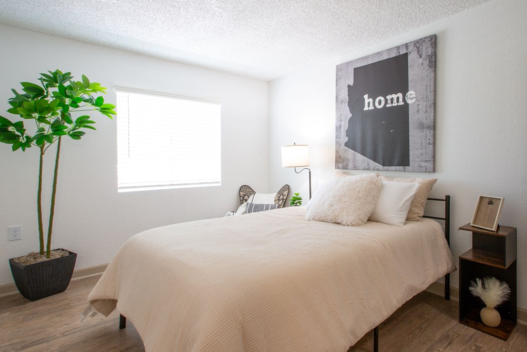 A bedroom with a bed, a potted plant, a lamp, and a framed picture on the wall.