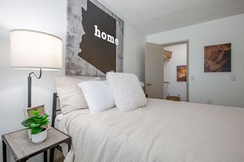 A bedroom with a bed, lamp, and a picture of a woman.