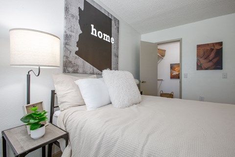 A bedroom with a bed, lamp, and a picture of a woman.