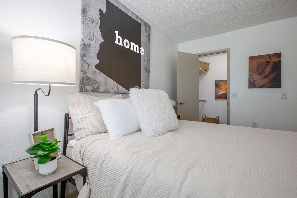 A bedroom with a bed, lamp, and a picture of a woman.