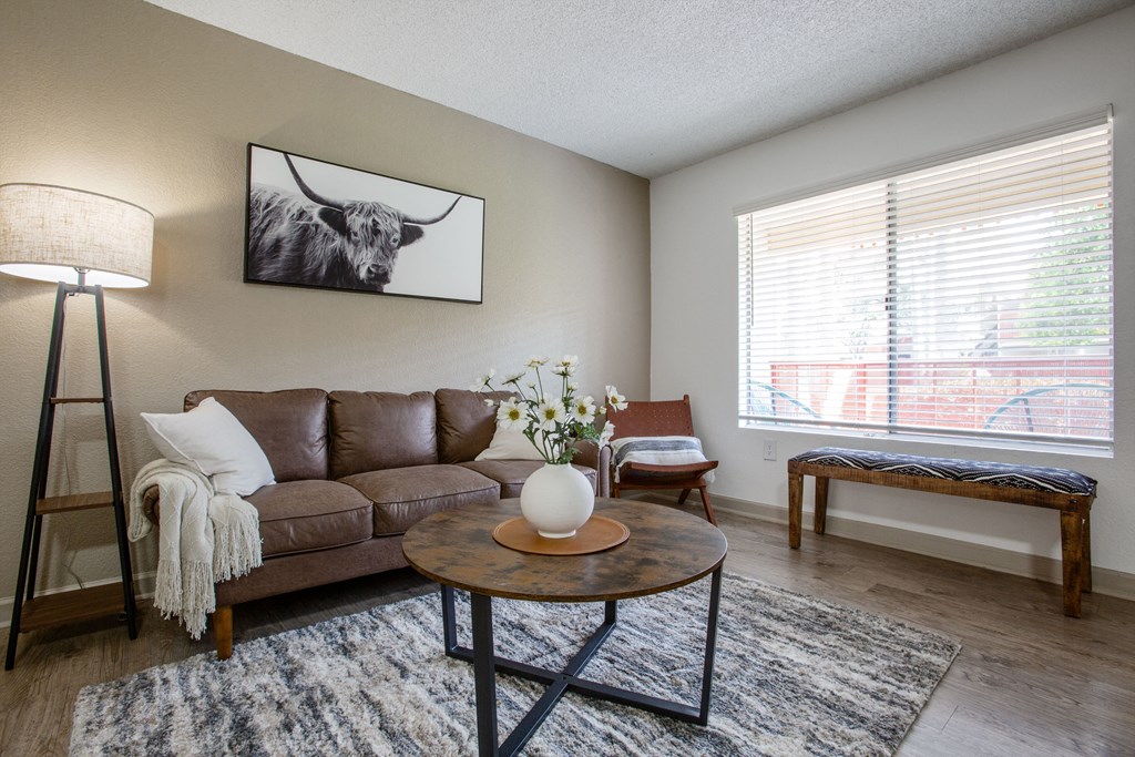 A living room with a brown leather couch, a coffee table, and a painting of a cow on the wall.