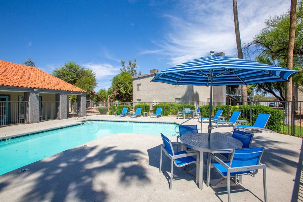A blue umbrella shades a table with four chairs around a pool.