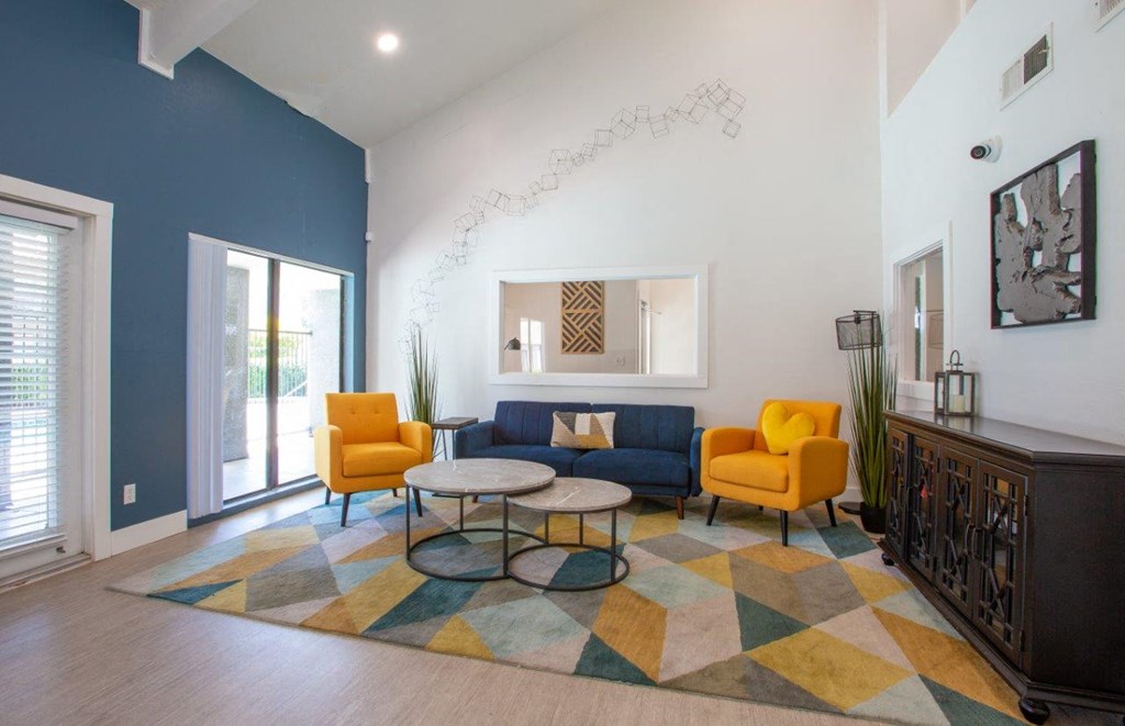 A living room with a blue couch, yellow chairs, and a colorful rug.