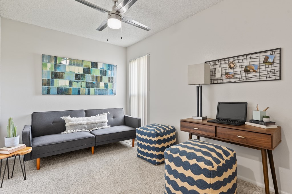 A living room with a grey couch, a wooden desk, and a ceiling fan.