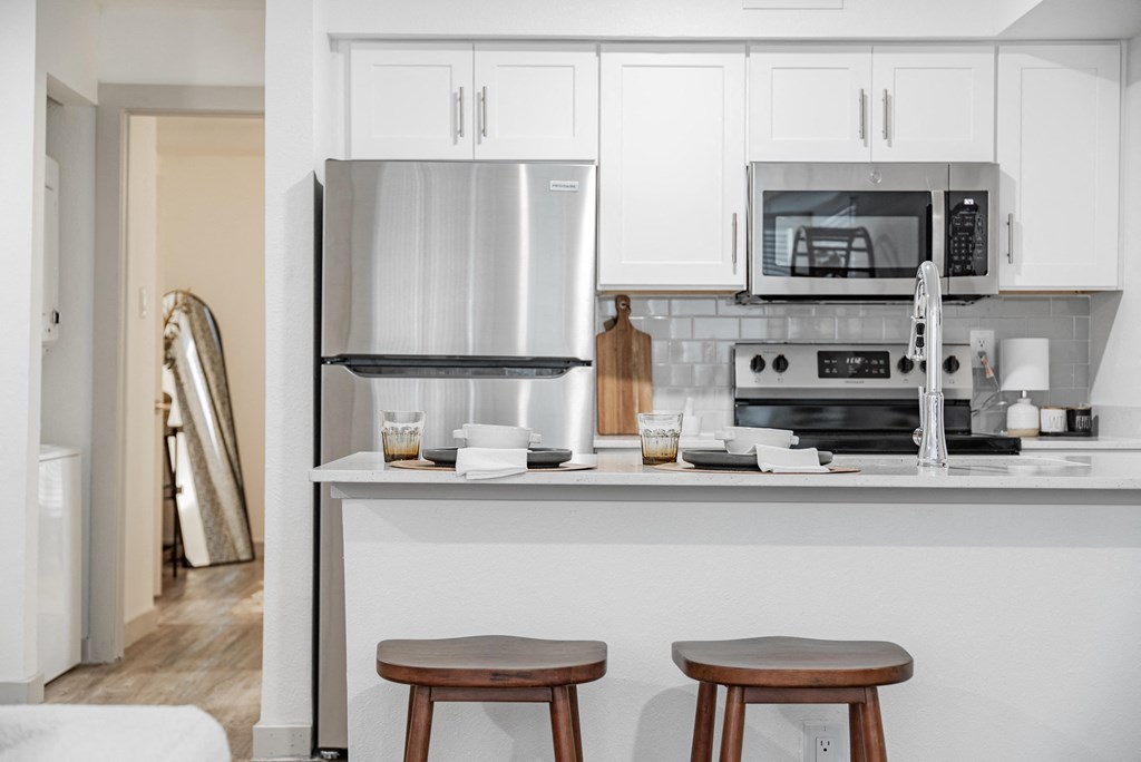a kitchen with white cabinets and a counter with two stools