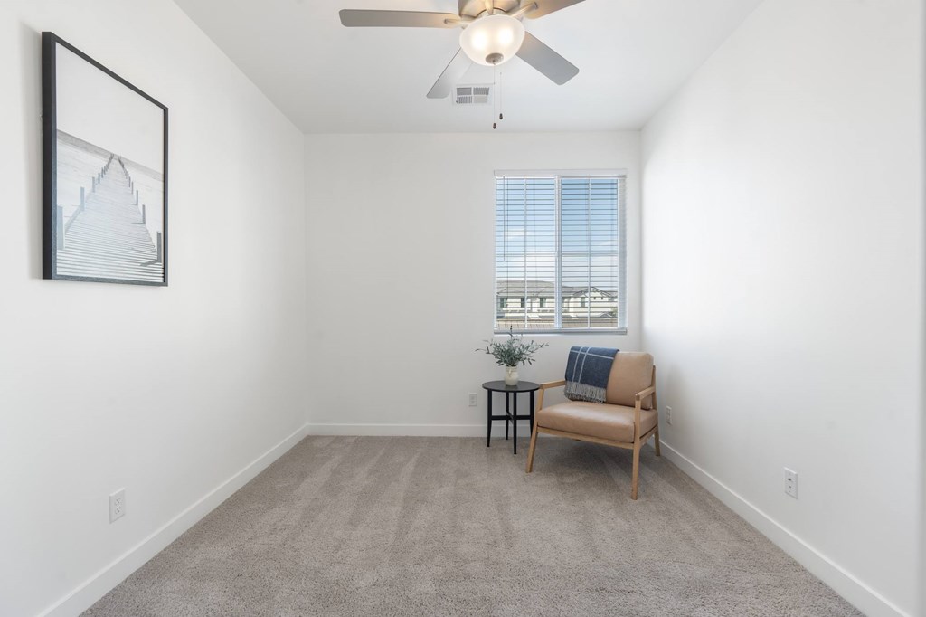 A room with a ceiling fan, a chair, and a small table with a plant on it.