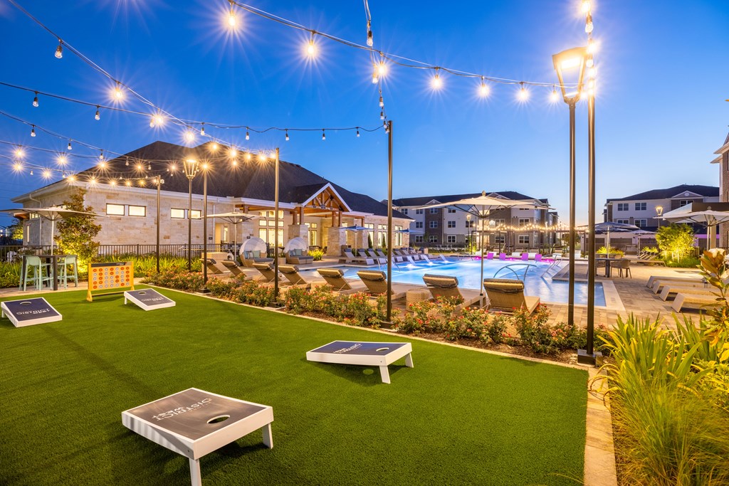 a backyard with a pool and lounge chairs under string lights