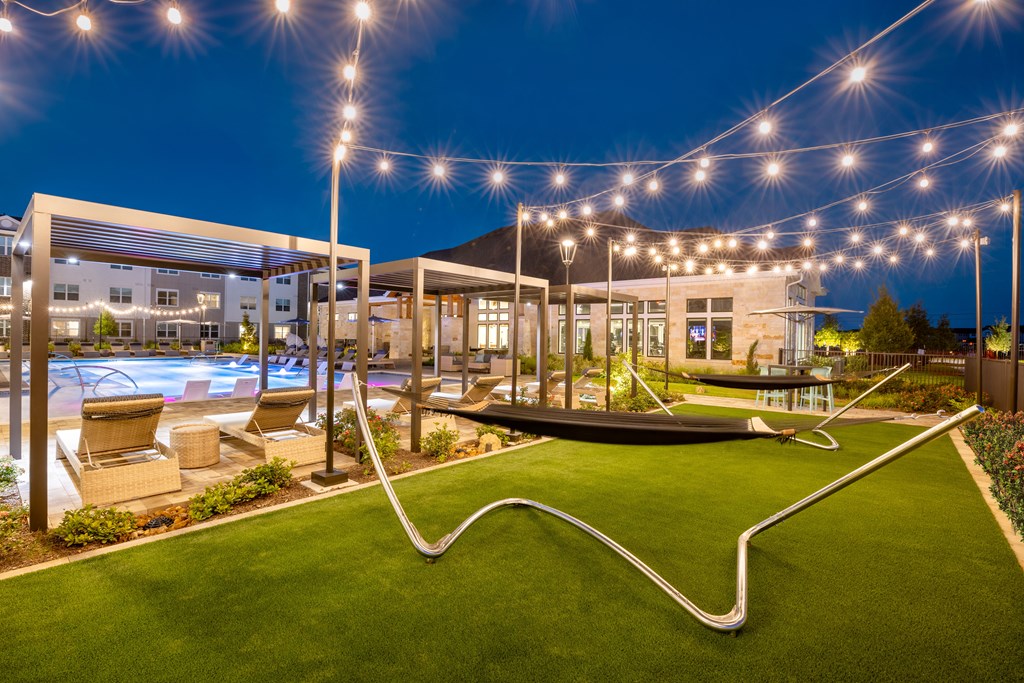 a view of the outdoor pool at night with string lights and a hammock in the middle