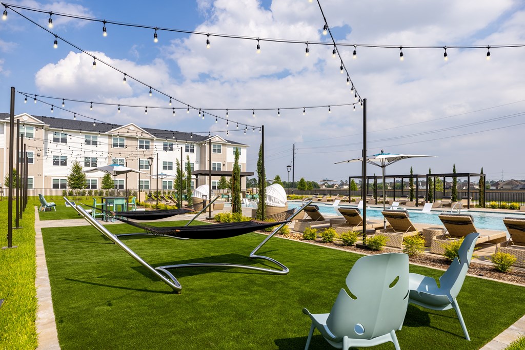 a grassy area with hammocks and lounge chairs and a pool in the background