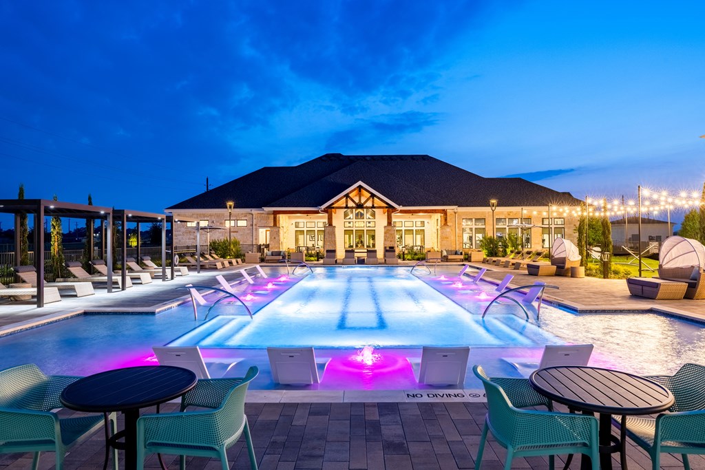 a pool with blue and green chairs and a building in the background