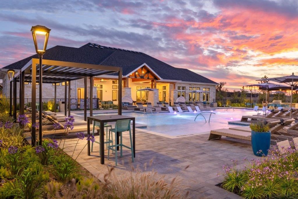 a pool with lounge chairs and a building with a sunset in the background