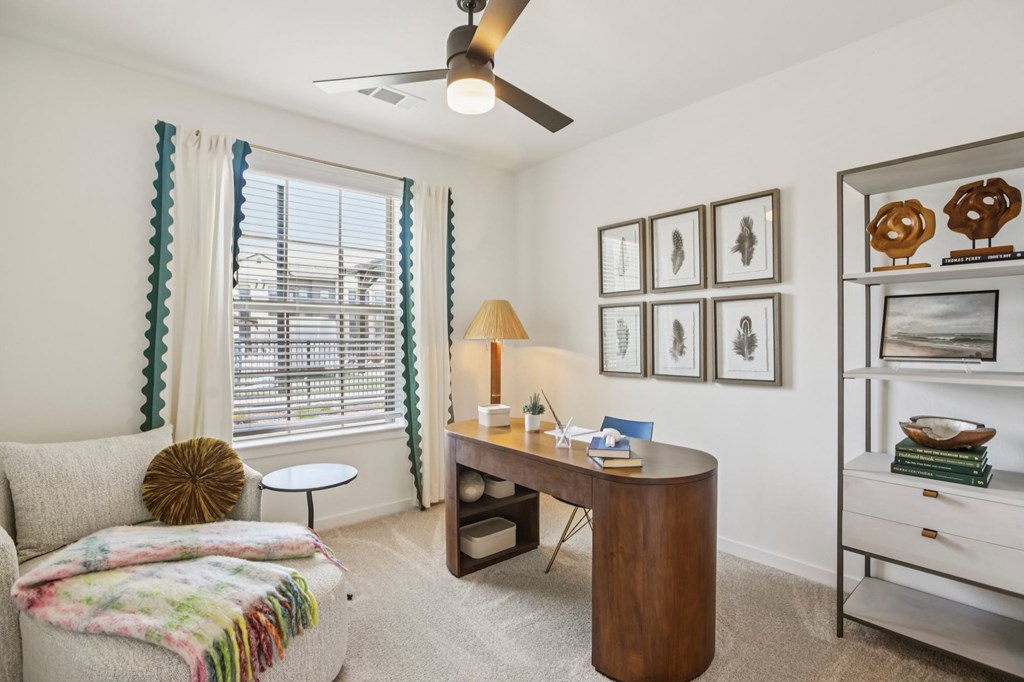 A room with a couch, a desk, and a fan.