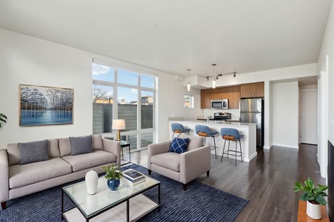 A living room with a grey couch, a glass coffee table, and a painting on the wall.