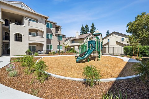 A playground with a green slide is surrounded by a white fence and brown mulch.