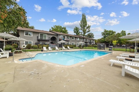 A large swimming pool surrounded by lounge chairs and umbrellas in front of a building.