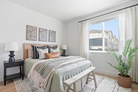 A bedroom with a bed, two lamps, a bench, and a potted plant.