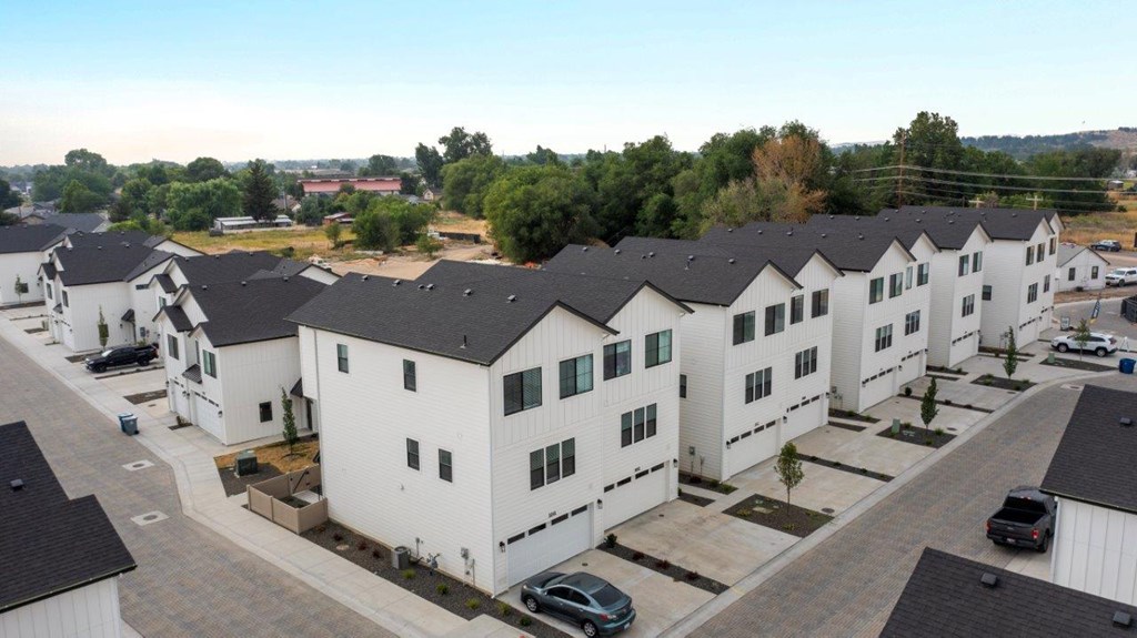 A row of white houses with black roofs and cars parked in front.
