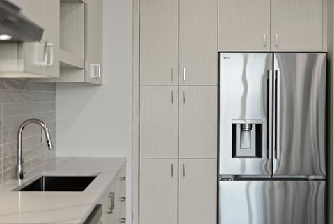 A modern kitchen with a stainless steel refrigerator and white cabinets.