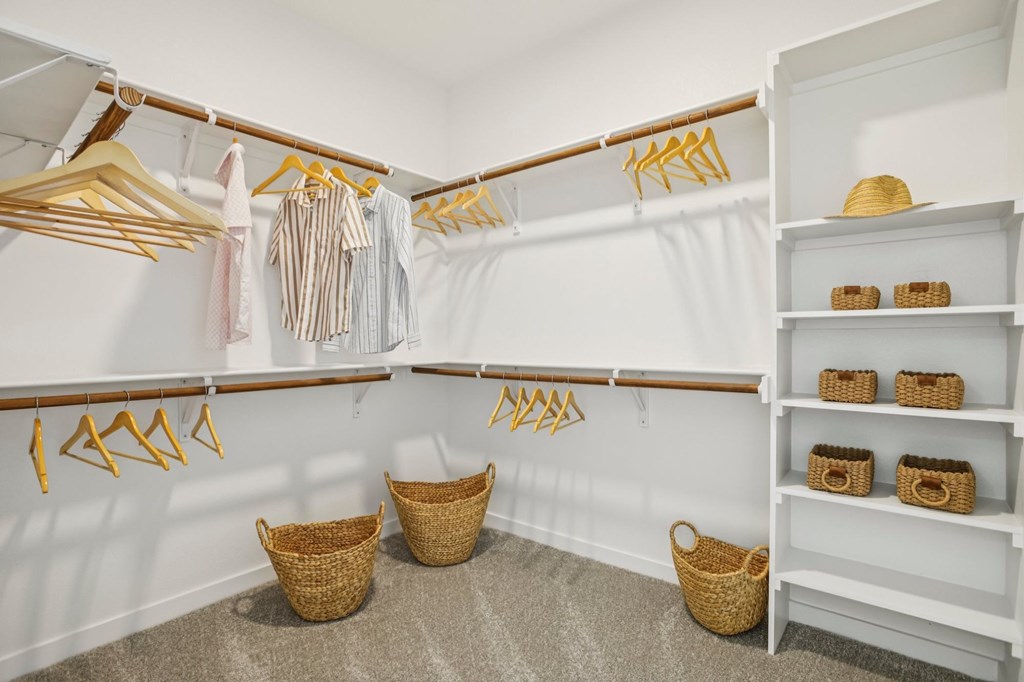 A white closet with clothes hanging and baskets on the floor.