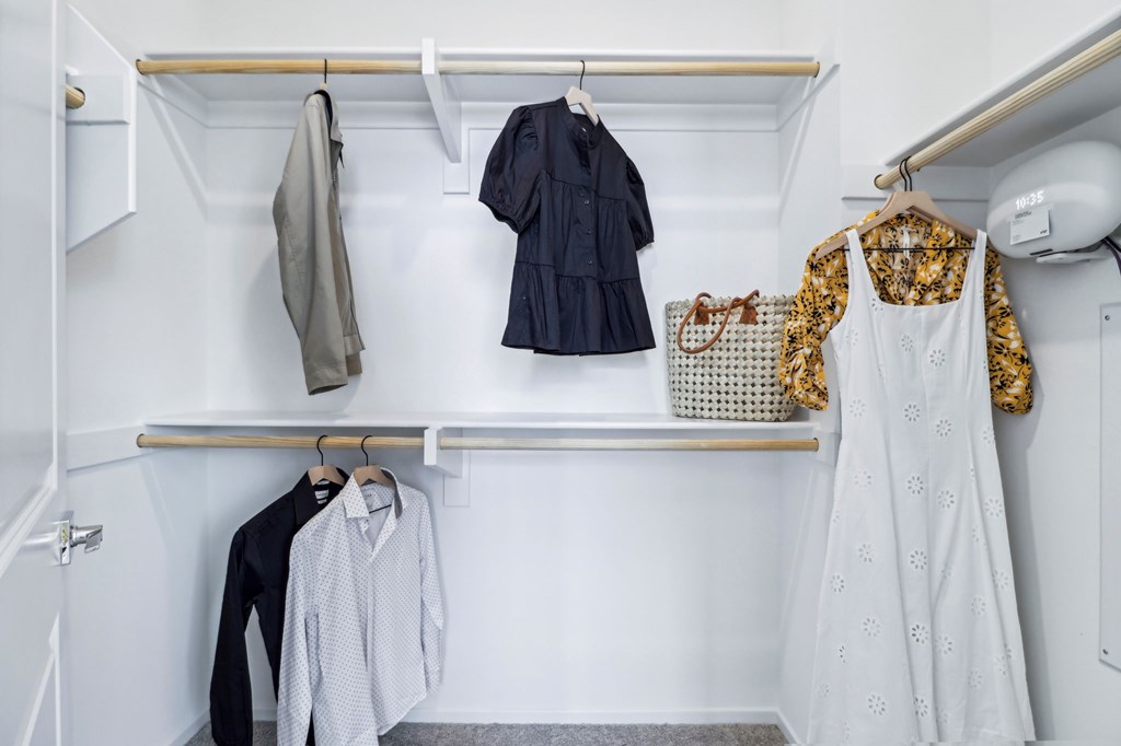 A white closet with clothes hanging on a rail.