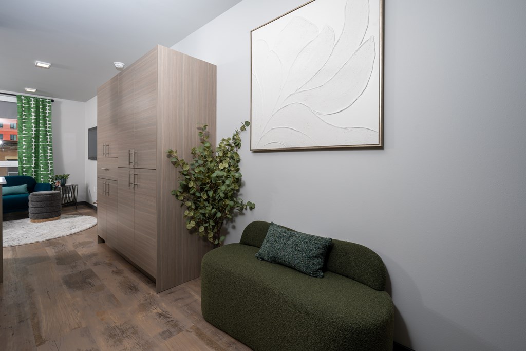 A green couch sits in front of a wooden cabinet and a white abstract painting.