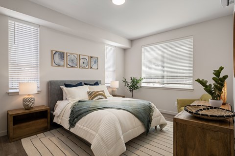 A bedroom with a bed, nightstand, and a plant.