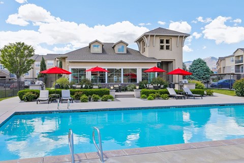 A large swimming pool in front of a house with red umbrellas.