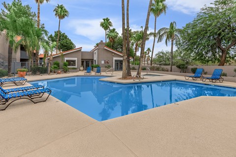 A pool surrounded by palm trees and a house in the background.